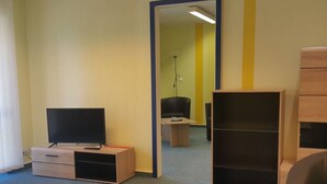 A room with a television on a wooden stand, a desk with a chair, and a large wardrobe.