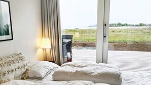 A bedroom with a bed, a nightstand, a lamp, and a view of a grassy area outside. - Luxury Seaside Retreat - By Traum Ferienwohnungen (Haderslev)