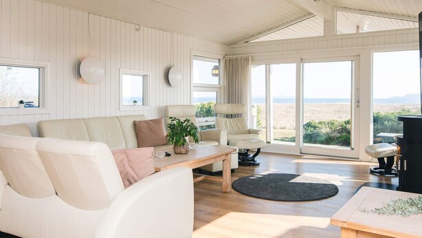 A spacious living room with a white sofa, a wooden coffee table, and a view of the outdoors through large sliding glass doors. - Luxury Seaside Retreat - By Traum Ferienwohnungen (Haderslev)