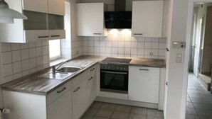 A compact kitchen with white cabinets, a built-in oven, a sink, and a stove. - Dat Onnen's Hus - Burhave 16 (Butjadingen)