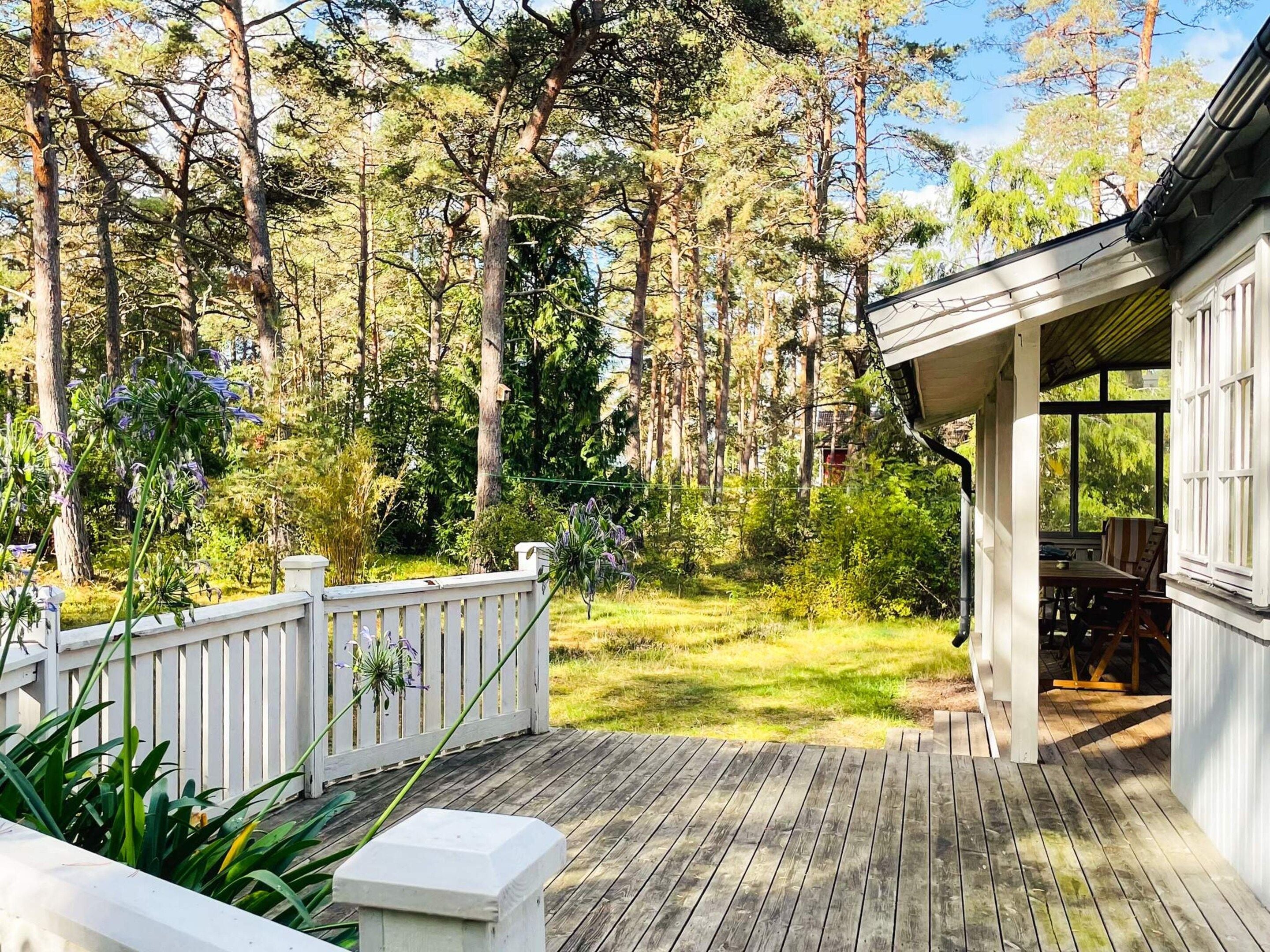 A wooden deck with a white railing, surrounded by a forested area.