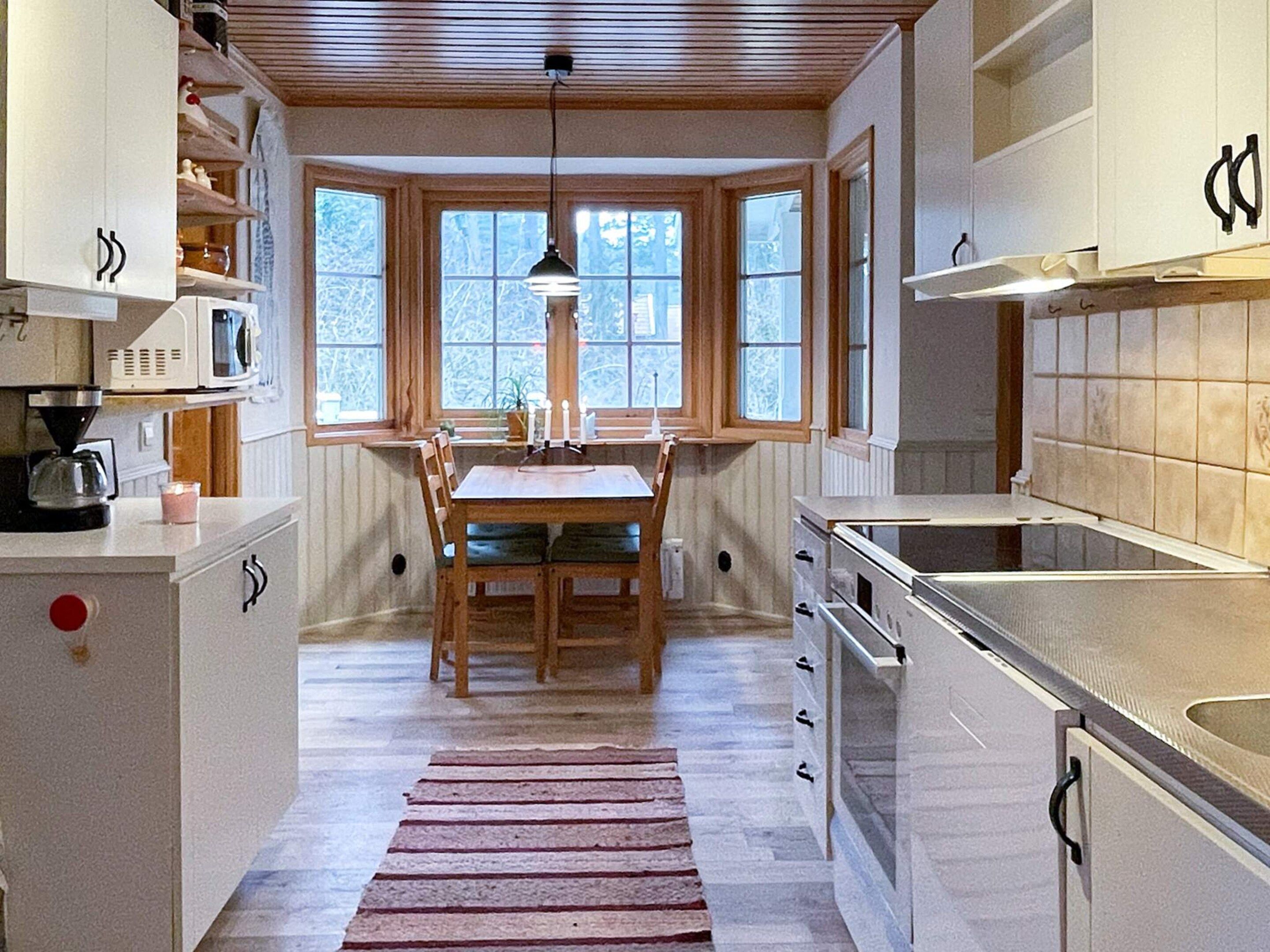 Una cocina con armarios de madera, una mesa de comedor y un ventanal con vista a árboles.