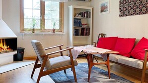 Un salon avec une cheminée, un canapé avec des coussins rouges, une table basse en bois et une bibliothèque.
