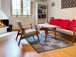 A living room with a fireplace, a sofa with red cushions, a wooden coffee table, and a bookshelf. - 6 Person Holiday Home in Yngsjo (Yngsjo)
