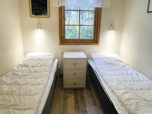 A small, single-room bedroom with two single beds, a wooden dresser, and a window with a view of greenery outside. - 6 Person Holiday Home in Yngsjo (Yngsjo)