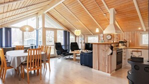 A spacious living area with a wooden ceiling, a dining table, and a kitchen area with a stove.
