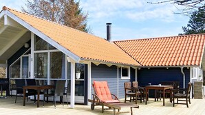 A covered outdoor area with a wooden deck, a glass enclosure, and a blue building with a red-tiled roof.