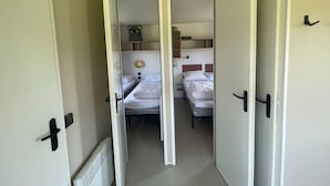 A narrow hallway leading to a bedroom with two beds, a radiator, and a door with a black handle. - Lovely Chalet in Schoonloo With Patio (Schoonloo)