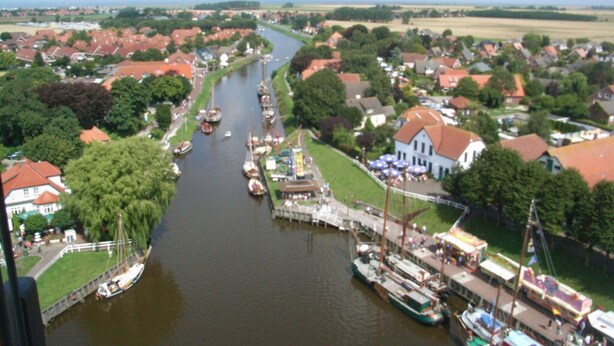 A river with boats docked along the banks, surrounded by residential houses and greenery. - Holiday Apartment Maschke (Wittmund)