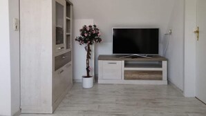 A room with a wooden wardrobe, a television on a wooden stand, and a potted plant. - Holiday Apartment Maschke (Wittmund)