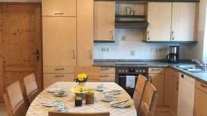 A compact kitchen with wooden cabinets, a dining table set for four, and a coffee maker. - Ferienhof Schonmetzler (Altusried)