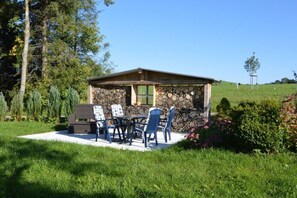 A stone building with a covered patio, outdoor seating, and a view of a green field. - Ferienhof Schonmetzler (Altusried)
