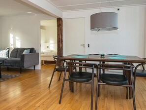 A modern living room with a wooden floor, a grey sofa, a dining table with chairs, and a large window. - Holiday Home on a Holiday Park in Ebeltoft (Ebeltoft)