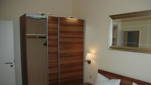 A hotel room with a bed, a wooden wardrobe, a mirror, and a wall-mounted lamp. - Holiday Apartment Villa in the Park (Wangerooge)