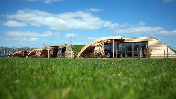 A modern building with a curved roof and large windows, situated on a grassy field. - Peaceful Farmside Bungalow (Heeten)