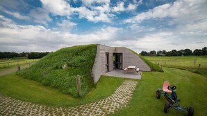 A modern house with a grass-covered roof, a paved pathway, and a tricycle in the foreground. - Peaceful Farmside Bungalow (Heeten)