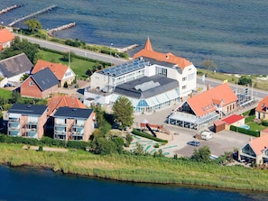 An aerial view of a coastal town with a mix of residential and commercial buildings, including a prominent hotel with a large glass facade and a restaurant with outdoor seating. - 6 Person Holiday Park Home in Hejls (Hejls)
