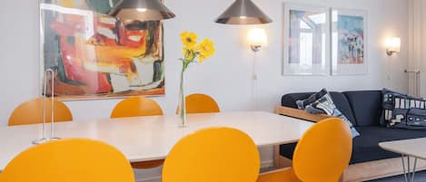 A dining area with a white table, yellow chairs, and two pendant lights.