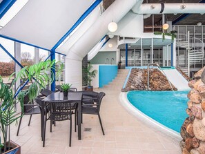 Una piscina interior con pared de piedra, un tobogán y una zona de estar con sillas y una mesa.