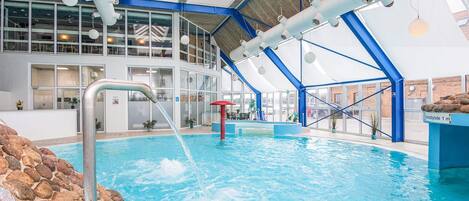 An indoor swimming pool with a clear view of the roof structure, a lifeguard stand, and a stone border around the pool.