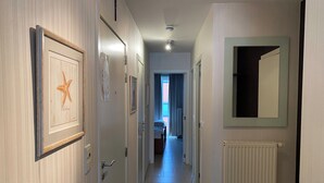 Ein Flur mit gerahmten Kunstwerken, einem Heizkörper und einem Spiegel an der Wand.