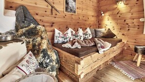 A rustic cabin interior with a wooden bed, pillows, a woven rug, and a stone fireplace. - Felsenhutte Modern Retreat (Graen)