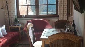 A cozy room with a wooden ceiling, a large window, a red sofa, a wicker chair, a small table, and a floor lamp. - Appealing Apartment in Lenzkirch (Lenzkirch)