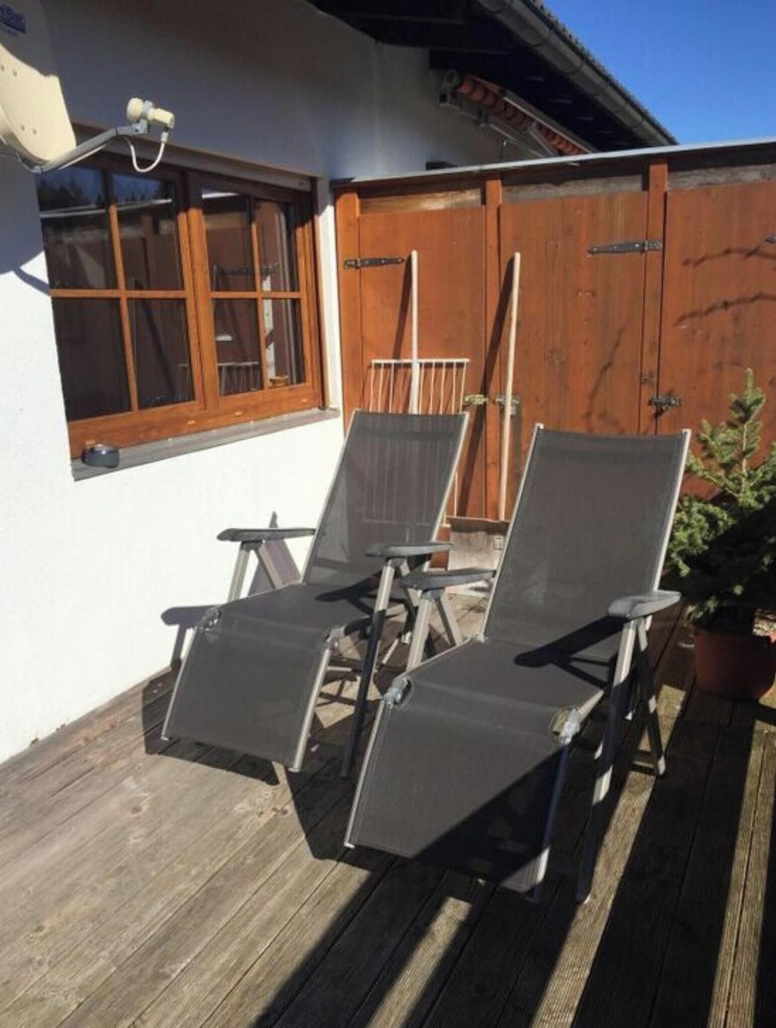 Eine Terrasse mit zwei Liegestühlen, einem kleinen Tisch, einem Holzzaun und einem Blumentopf.
