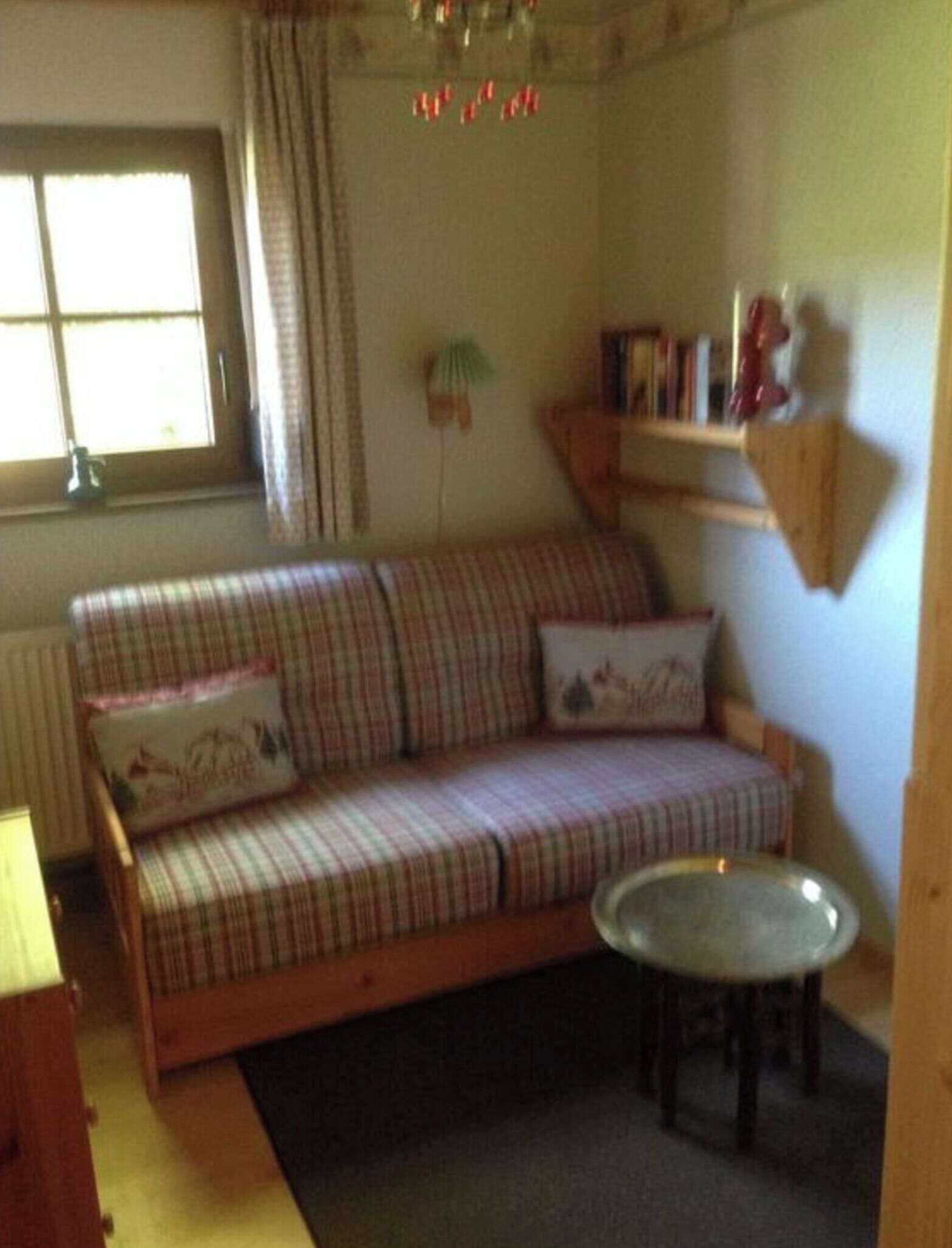 Ein gemütliches Wohnzimmer mit einem Karo-Sofa, einem kleinen runden Tisch und einem fenster mit Vorhängen.