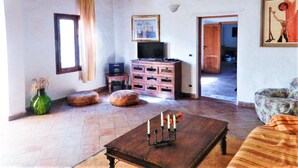 A living room with a wooden coffee table, ottomans, a television, and a painting on the wall. - Delightful Holiday Home in Fulgatore With Swimming Pool (Erice)