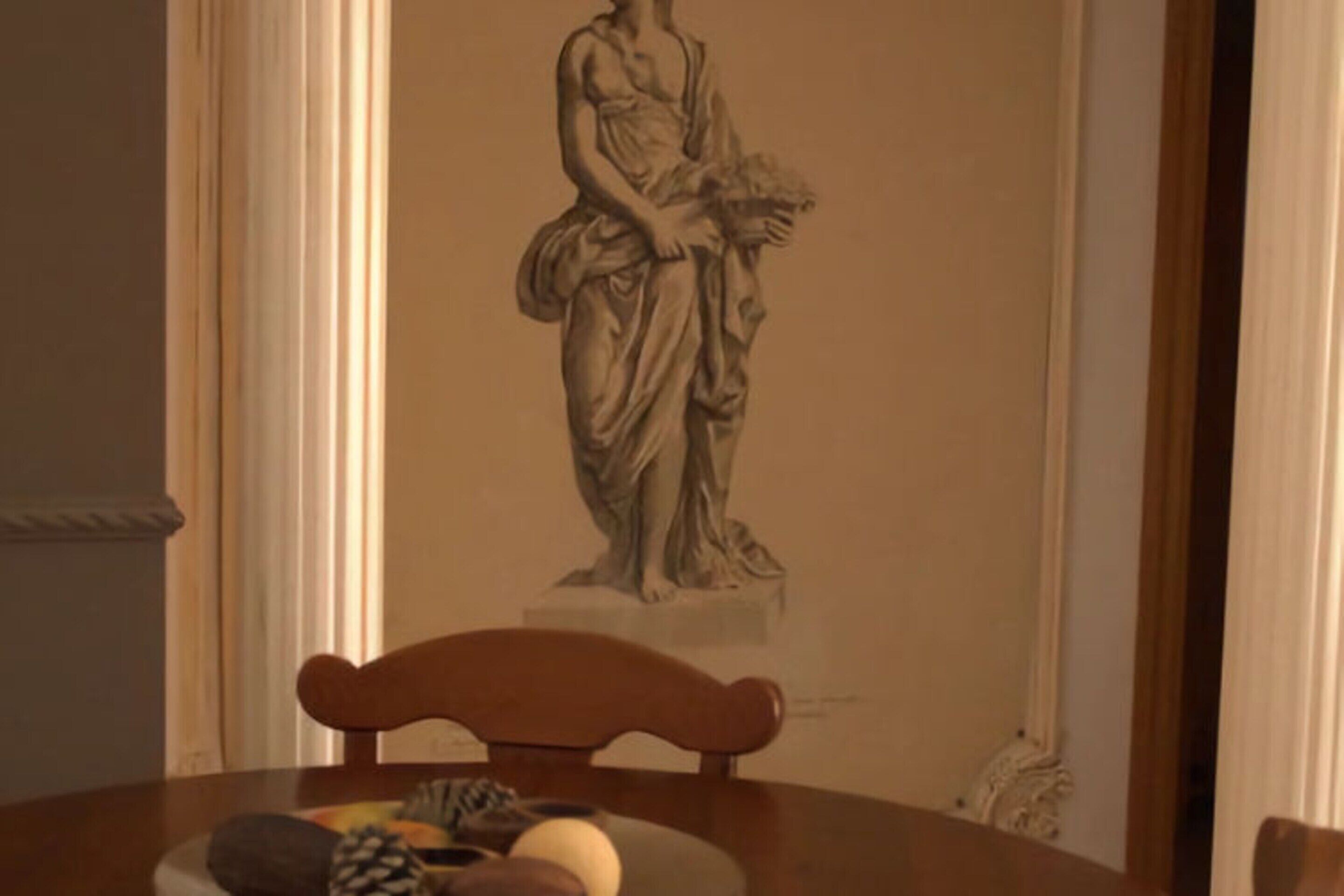 A dining table with a statue of a woman holding a bouquet, a wooden chair, and a fruit bowl.