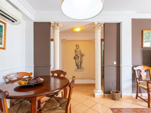 A dining area with a round wooden table, two wooden chairs, a wicker chair, a statue on the wall, and a tiled floor. - Apartment in Nerja Near Sea Beach (Nerja)