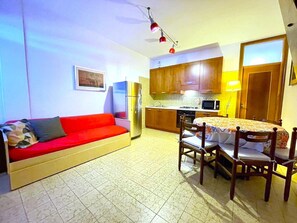 A compact living space with a kitchenette, a dining area with chairs, a sofa, and a refrigerator.