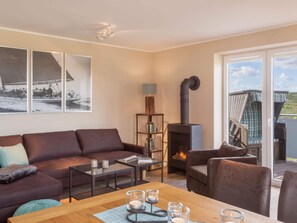 A cozy living room with a brown leather sofa, a wooden coffee table with candles, and a fireplace. There are three framed pictures on the wall and a bookshelf with a lamp. - Dunenhuus Ost Modern Retreat (Juist)