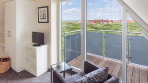 Un balcon donnant sur un paysage côtier, un meuble TV blanc et une table en verre.