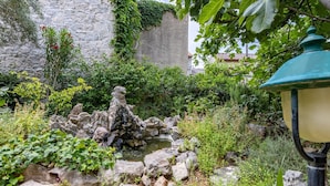 A garden with a stone fountain, lush greenery, and a lamp post. - Stylishly Decorated Apartment With Private Terrace (Punat)