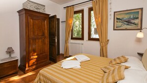 A bedroom with a bed, a wooden wardrobe, a radiator, a window with curtains, and a painting on the wall. - Hillside Pool & Spa Retreat (Castagneto Carducci)