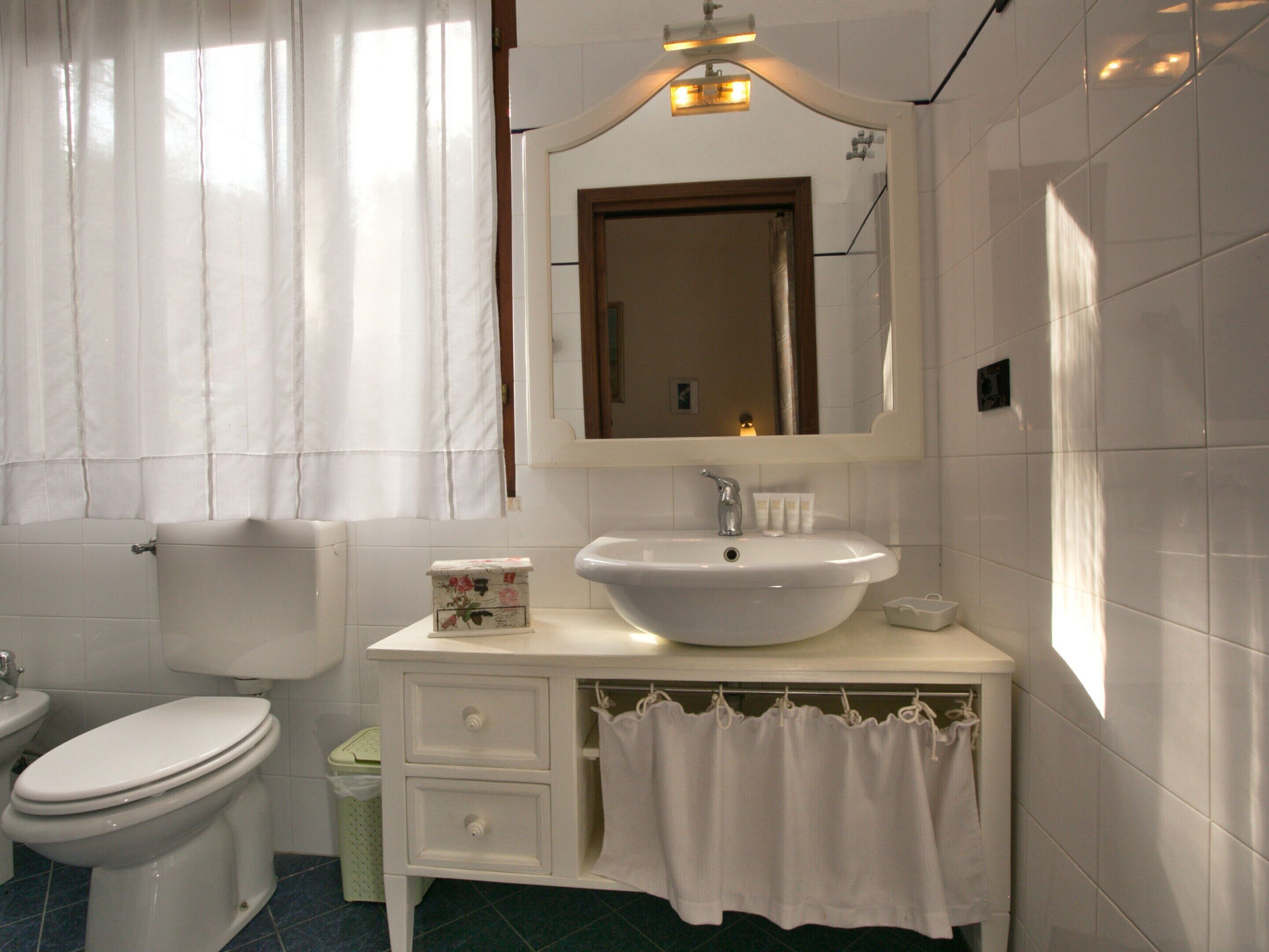 Un baño con lavamanos blanco, inodoro, espejo y cortina de ducha.