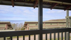 Blick von einem überdachten Balkon auf einen Strand, im Hintergrund mehrere Gebäude.