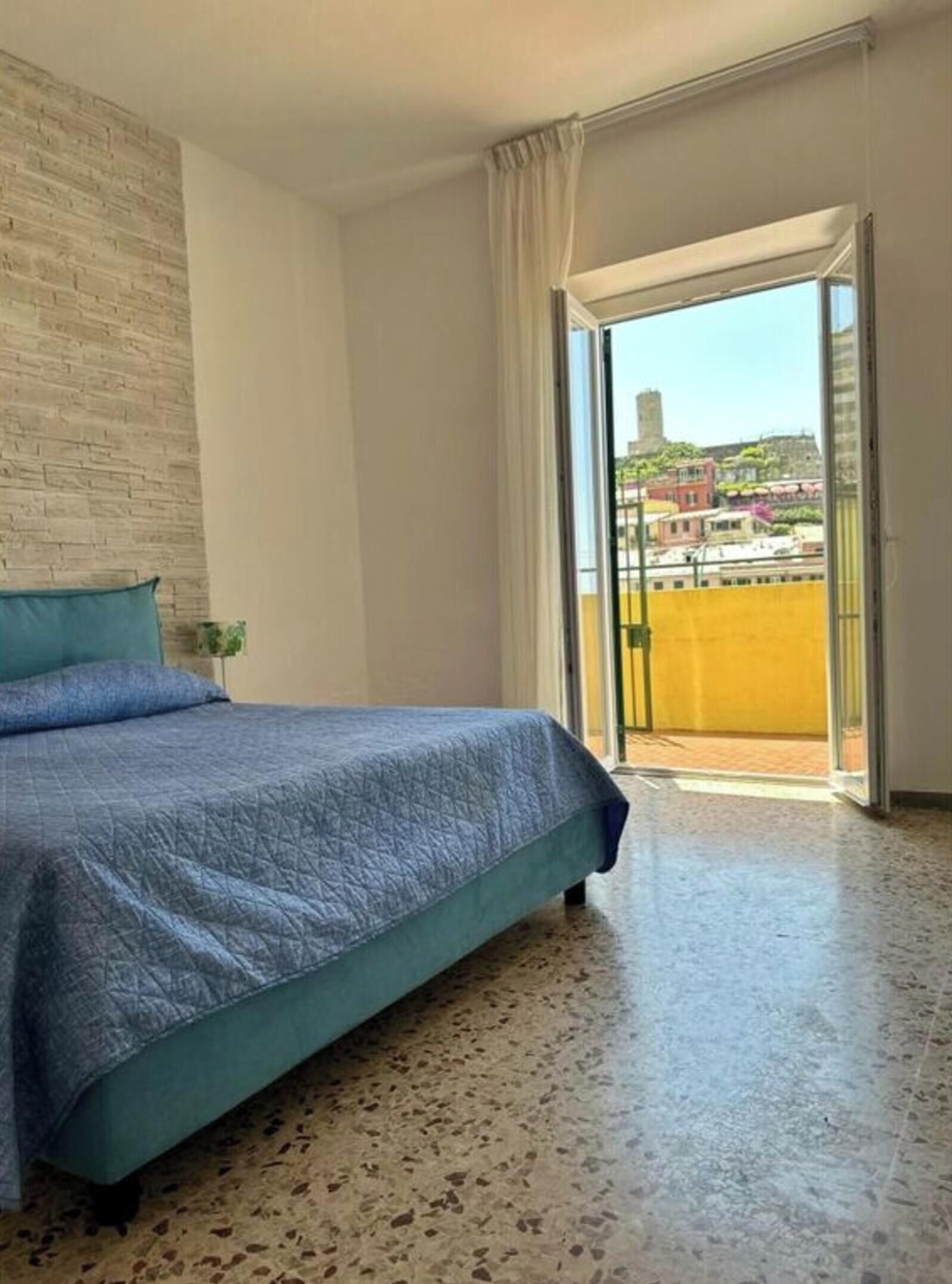 A bedroom with a bed, a window, and a view of buildings outside.