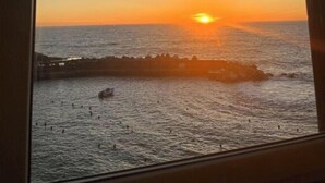 A sunset view through a window, with the sun setting over the ocean and a pier in the distance. - La Casa sul Mare (Vernazza)