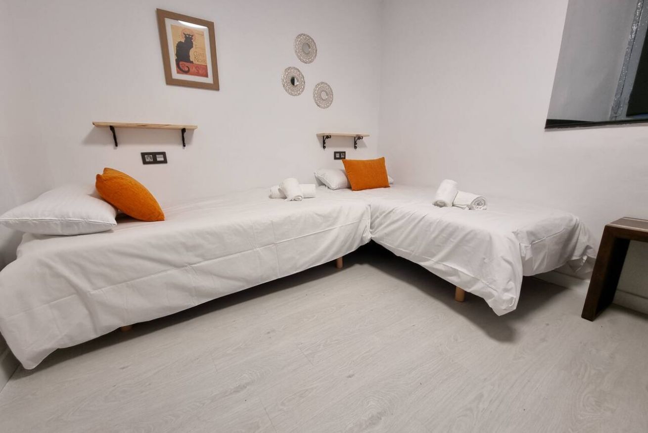 Ein Zimmer mit zwei Betten, weißer Bettwäsche, orangefarbenen Kissen, Holzboden und Wandregalen.