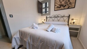 A neatly made bed with white linens and towels, a metal headboard, bedside tables with lamps, and a window with a view.