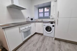 Une cuisine compacte équipée d’un four à micro-ondes, d’un four traditionnel, d’un lave-linge et d’une fenêtre donnant sur un paysage agréable.