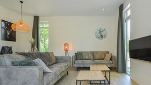 A modern living room with two sofas, a coffee table, a TV, and a large window with curtains. - Lovely Apartment in Wolpinghausen (Zorgvlied)