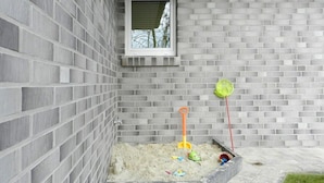 A small outdoor play area with a sandbox, a window, and a brick wall. - Holiday Apartment Deck Boat (Butjadingen)