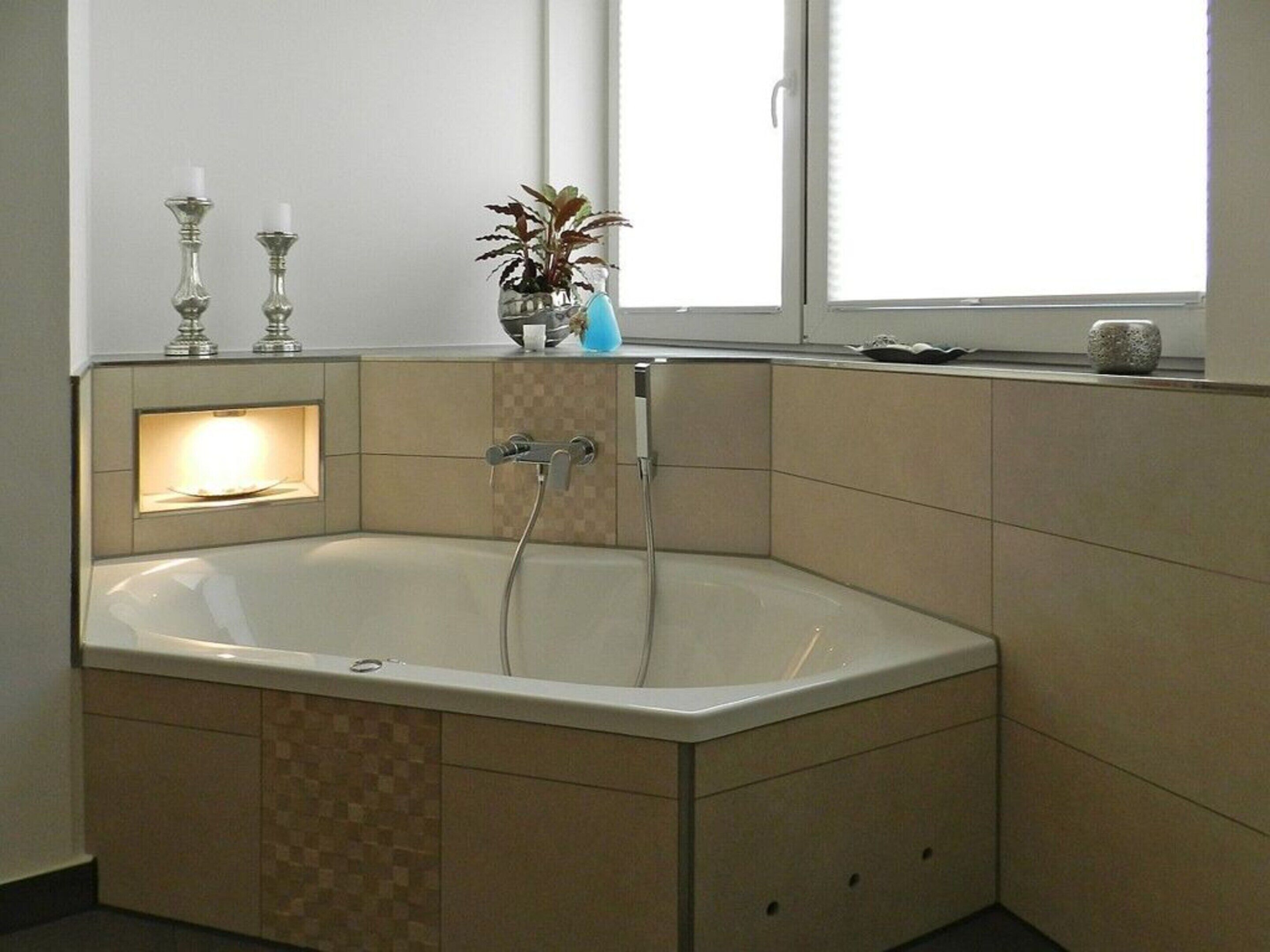 Un baño en esquina con una bañera independiente, un ventanal pequeño y una planta en el alféizar.