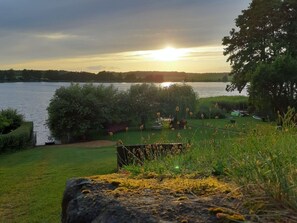 Une vue sur le lac, avec une zone herbeuse, des arbres et un rocher au premier plan.