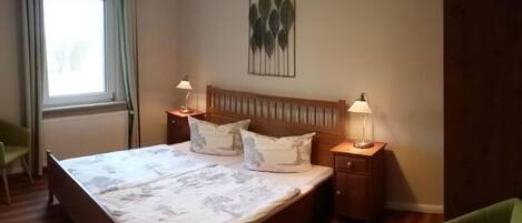 A neatly arranged bedroom with a wooden bed, two bedside tables with lamps, a green chair, and a window with curtains.