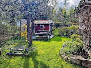 Una casa de madera roja con un pequeño porche, rodeada de un jardín bien cuidado con diversas plantas y flores.